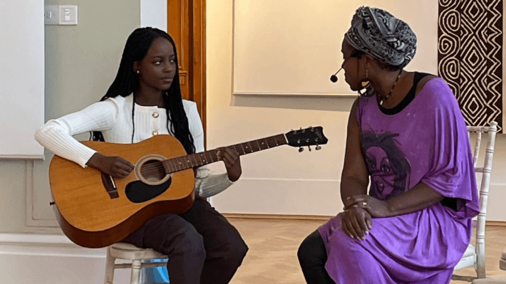 Two women, one is singing and the other playing a guitar