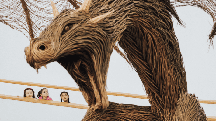 a wicker dragon and three young girls staring at it